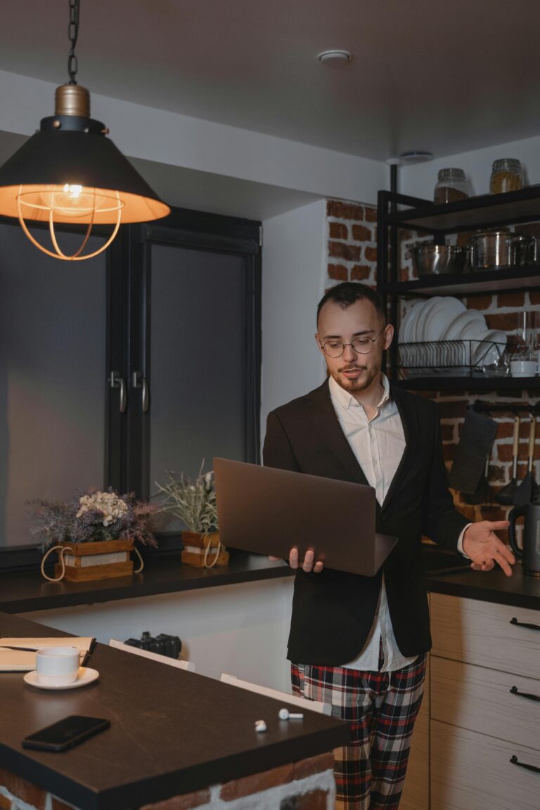 A man in a suit working remotely in a cozy kitchen setting, using a laptop.